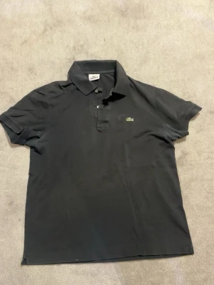 Lacoste pikétröja svart – Strl M - Säljer en klassisk Lacoste pikétröja i svart med den ikoniska krokodilloggan på bröstet. Stilren och tidlös modell som passar både till vardags och finare tillfällen.  📏 Storlek: M ✅ Original Lacoste ✅ Fint skick ✅ Klassisk passform ✅ Broderad krokodillogga