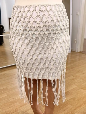 Vit kjol med makramé och fransar - Superfin vit kortkjol med makramé-detaljer och långa fransar nertill. Kjolen har en tajt passform och ett unikt nätmönster som ger en bohemisk vibe. Perfekt för dig som vill sticka ut med en trendig och cool look. Inte använd en enda gång! Och är i storlek S men är jätte stretchig passar även om du har storlek M