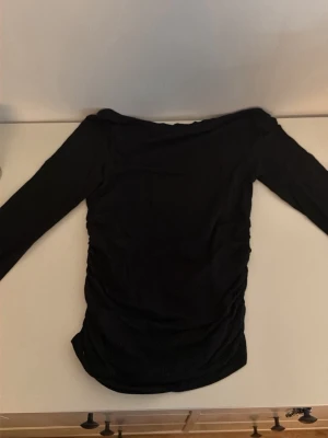 Svart långärmad topp - En svart långärmad topp med enkel och stilren design. Toppen har en kroppsnära passform och är tillverkad i ett mjukt material som känns bekvämt mot huden. Perfekt att matcha med jeans eller kjol för en clean look.