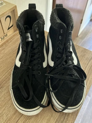 Svarta Vans  - Klassiska Vans i svart mocka och textil med vit sula. Högt skaft med mjuk, fluffig fodring runt ankeln och svarta skosnören. Dom har blivit använda några gånger men dom ser nästa nya ut 