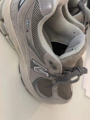 Grå New Balance 2002R sneakers - Snygga New Balance 2002R sneakers i olika grå nyanser med mesh och mocka på ovandelen. Klassisk N-logga på sidan och snörning framtill. Skorna har en chunky sula och sportig vibe, perfekta för dig som gillar streetwear.