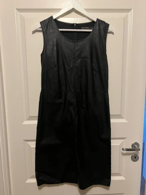 Svart ärmlös klänning från Soya Concept - Snygg svart ärmlös klänning från Soya Concept i skinnimitation. Klänningen har rund halsringning och dragkedja bak. Perfekt för dig som vill ha en stilren och edgy look.