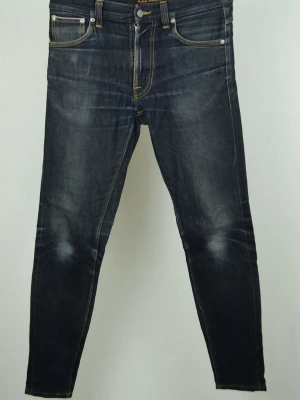 Nudie Dry true selvage  - NUDIE DRY TRUE SELVAGE JEANS Storlek : 30/32 Modell : Lean Dean Mått : A = 42CM - B = 102CM - C = 14CM Användning : Jeansen är i ett fint skick men börjat "dra" lite vid sömmarna Nypris : Cirka 2700SEK Modellen på bilden : 182CM och väger 73,5KG