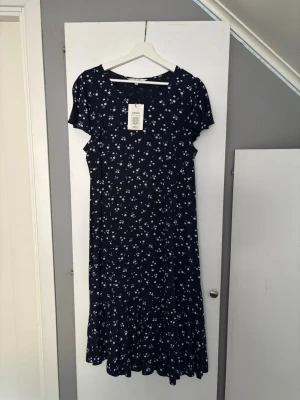 Marinblå klänning  - Marinblå långklänning från Cellbes med blommor. Klänningen har volanger vid ärmar och längst ner på klänningen. Super skönt material. Storlek 42/44 men skulle säga mer som 40 (M)