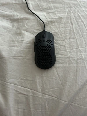 HyperX svart gamingmus med hål - Säljer en svart gamingmus från HyperX med honeycomb-design för extra låg vikt. Musen har sladd, scrollhjul och flera knappar. Tillverkad i plast med matt finish och vita glidytor undertill. Perfekt för snabba rörelser och gaming sessions.