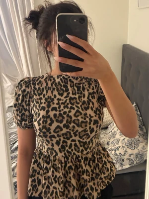 Leopardmönstrad topp med puffärm - Säljer en leopardmönstrad topp med puffärmar och volang nedtill. Toppen har snygga knytband i ryggen. Aldrig använt plagget!!!