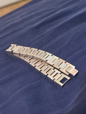Silverfärgat länkarmband i metall - Säljer ett stilrent silverfärgat armband med breda länkar i metall. Armbandet har rektangulära länkar med snygga mönstrade detaljer på vissa av dem. Perfekt för dig som gillar en modern och clean look.