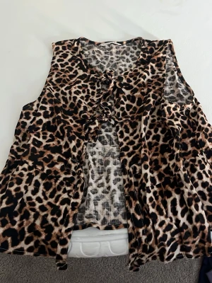 Leopardmönstrad väst med snörning - Säljer en leopardmönstrad väst med snygga snörningsdetaljer framtill. Västen är ärmlös och har en loose passform, perfekt för att addera lite edge till din outfit. Materialet känns mjukt och lätt, och mönstret är riktigt iögonfallande.