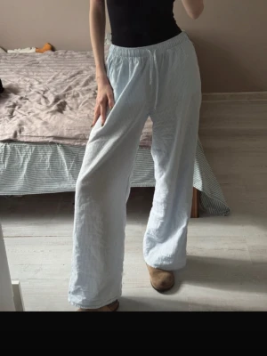 Randiga ljusblå loungewear-byxor - Säljer ett par lösa och bekväma loungewear-byxor i ljusblått med tunna vita ränder. Byxorna har resår och dragsko i midjan samt vida ben. Perfekta för chill dagar hemma.