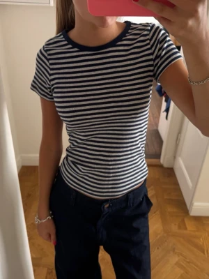 Randig blåvit t-shirt med tight passform - Säljer en stilren t-shirt med marinblå och vita ränder. T-shirten har korta ärmar, rund halsringning och sitter tight mot kroppen. Perfekt för dig som gillar en klassisk och enkel look.