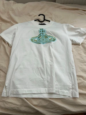 Vit t-shirt Vivienne Westwood - Säljer en vit t-shirt från Vivienne Westwood Anglomania med det ikoniska orb-logotrycket i blått och grönt framtill. Klassisk passform och rund halsringning. Perfekt för dig som vill ha något stilrent men ändå sticker ut.