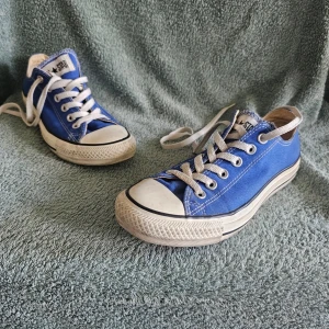 Blå Converse All Star låga sneakers - Klassiska blå Converse All Star sneakers med vit tåhätta och vita snören. Skorna har lågt skaft och är tillverkade i canvas med gummisula. Perfekta för en avslappnad och cool stil.