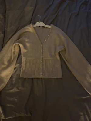 Beige kofta från Gina Tricot - Mysig beige kofta från Gina Tricot med v-ringning och knappar framtill. Koftan har långa stora ärmar. Knappt använd men lite knoppigt material. Annars fint skick!!❤️❤️