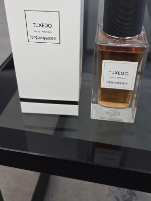Yves Saint Laurent Tuxedo parfym - Exklusiv parfym från Yves Saint Laurent, Tuxedo, med noter av kryddor och patchouli. Flaskan är rektangulär i tjockt, genomskinligt glas med svart kork och elegant vit etikett. Kommer i stilren vit kartong med svart detalj. Perfekt för dig som gillar lyxiga dofter.