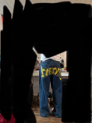 Blå baggy jeans från Junkyard  - Säljer ett par blå jeans från Junkyard i storlek M. Jeansen har ett stort gult tryck med texten 'yard' över bakfickorna och raka ben. Klassisk femficksmodell i denim med synliga sömmar och rå kant nedtill. Perfekta för dig som gillar streetwear och statement-plagg. Säljer för ja har bytt stil, har andvänt dom en gång. Nypris 800 om ja ibte minns fel