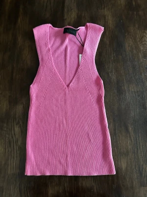 Rosa ribbad linnetopp från Zara - Snygg rosa ribbad linnetopp från Zara med djup v-ringning och ärmlös design. Toppen har en croppad passform och är tillverkad i ett mjukt, stretchigt material som sitter skönt på kroppen. Perfekt för att lyfta vilken outfit som helst. Ny pris 230