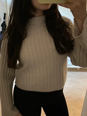 Beige ribbstickad tröja - Säljer en beige ribbstickad tröja med hög hals och långa ärmar. Perfekt att matcha med jeans eller kjol för en clean look!
