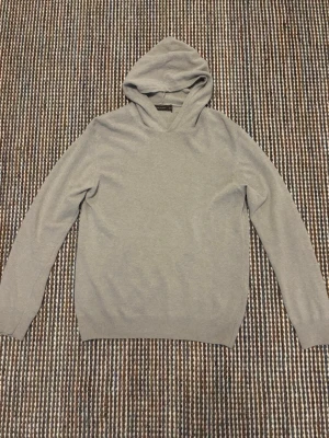 Beige Oscar Jacobson Kashmir Hoodie - En stilren ljusgrå hoodie från Oscar Jacobson i mjukt och tunt stickat kashmir. Klassisk modell med huva och långa ärmar, perfekt för en avslappnad look. Ribbstickade muddar vid ärmslut och nederkant ger en snygg passform.