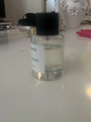 ESSNCE Cozy Goddess Eau de Parfum - Minimalistisk parfymflaska från ESSNCE med doften Cozy Goddess. Flaskan är genomskinlig med svart lock och vit etikett med svart text. Innehållet är en klar vätska. Perfekt för dig som gillar stilrena och moderna dofter.