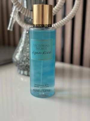 Victoria's Secret Aqua Kiss mist - Fräsch body mist från Victoria's Secret i doften Aqua Kiss. Flaskan är cylinderformad i genomskinligt blå plast med guldfärgat lock och text i guld och svart. Innehåller 250 ml och ger en lätt, uppfriskande doft.