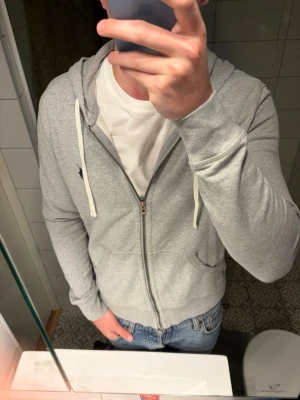 Ljusgrå hoodie med dragkedja - Snygg ljusgrå hoodie från Polo Ralph Lauren med dragkedja framtill och vit dragsko i huvan. Klassisk logga broderad på bröstet. Skriv för frågor! 