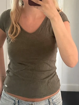 Olivgrön v-ringad t-shirt Hollister - Snygg olivgrön t-shirt från Hollister med v-ringning och korta ärmar. Ser ingen storlek men passar mig som har S, bra kvalité men lite urtvättad (lappen). 