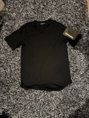 Balmain t-shirt  - Säljer en svart t-shirt från Balmain med rund hals och korta ärmar. På ena ärmen sitter en snygg patch-detalj i kontrasterande tyg med text. T-shirten har en clean look och är tillverkad i mjuk bomull.
