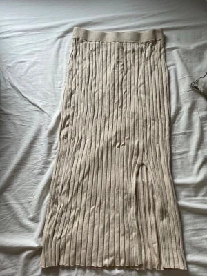 Beige ribbad långkjol från MONKL - Säljer en beige ribbad långkjol från MONKL i storlek S. Kjolen har en rak passform med slits framtill och är tillverkad i en mjuk mix av viskos och polyamid. Perfekt för dig som gillar stilrena och bekväma plagg med en modern twist.