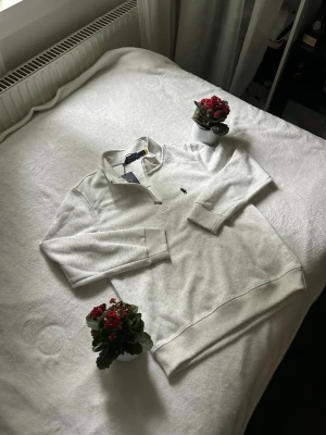 Ljusgrå halvzip från Polo Ralph Lauren - Snygg ljusgrå halvzip-tröja från Polo Ralph Lauren med klassisk krage och liten mörkblå logga broderad på bröstet. Tröjan har långa ärmar, ribbade muddar och är gjord i mjukt sweatshirtmaterial. Perfekt för en clean och avslappnad stil.