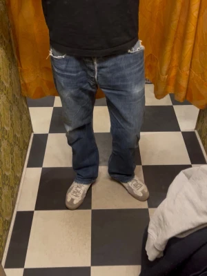 Vintage Levis 501 - Säljer ett par klassiska blåa Levis jeans med rak passform och slitningar på benet och fickorna. Jeansen har fem fickor, knappgylf och råa kanter vid bensluten. Perfekta för en avslappnad och trendig look. Det är bara höra av sig om ni har frågor!!!