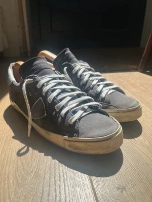 Blå sneakers från Philippe Model - Snygga blå sneakers från Philippe Model med vita detaljer och vita skosnören. Skorna har en låg silhuett och en beige, något sliten sula. Ovandelen är i mocka och läder, och hälen har en vit kontrast. Perfekta för en avslappnad streetstyle.