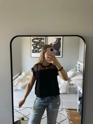 Svart t-shirt med meshdetalj - Säljer en svart ZARA t-shirt med korta ärmar och transparent mesh upptill vid axlar och hals. T-shirten har en enkel, loose passform och ger en cool och trendig vibe. Perfekt att styla med jeans eller kjol för en snygg look 🤍