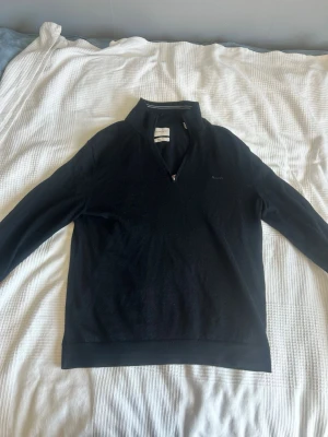 Svart halvzip-tröja från GANT - Snygg svart tröja från GANT med halvzip och hög krage. Diskret GANT-logga broderad på bröstet. Tillverkad i extra fin merinoull för en mjuk och bekväm känsla. Perfekt till jeans eller chinos för en clean look. Nypris: 1700                                                                      Fråga gärna om du har några vidare frågor!