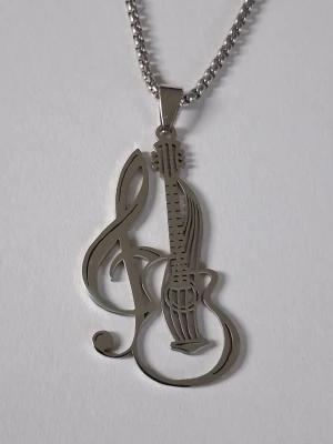 Halsband med gitarr och g-klav i stål - Snyggt halsband i silverfärgat stål med ett hängsmycke som föreställer en gitarr och en g-klav i ett stilrent, utskuret mönster. Perfekt för dig som älskar musik och vill ha en unik accessoar som sticker ut.