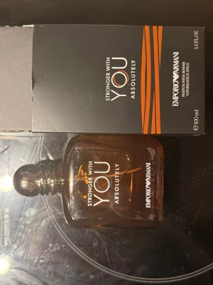 Emporio Armani Stronger With You - Emporio Armani Stronger With You Absolutely är en parfym i en elegant, mörkbrun glasflaska med rundade former och silverfärgad kork. Flaskan rymmer 100 ml och har en stilren design med vita och orange detaljer på etiketten och kartongen. Säljs med kvitto