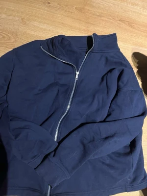 Mörkblå zip hoodie från 157 - Mörkblå hoodie med dragkedja.  Klassisk modell utan tryck, med hög krage och långa ärmar. Tillverkad i mjukt bomullsmaterial och har ribbade muddar vid ärmslut och nederkant. Perfekt för en chill och enkel stil. kragen kan man ha upp mot halsen men även vikt ner så den passar till olika tillfällen.