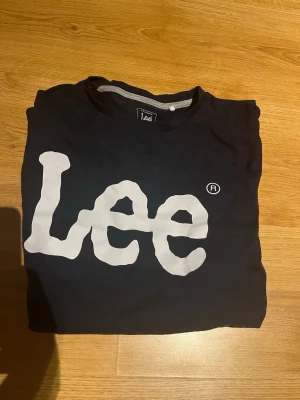 Svart Lee långärmad tröja - Säljer en svart långärmad tröja från Lee med stor vit logga framtill. Klassisk rund halsringning och regular fit. Perfekt för dig som gillar streetwear och vill ha en enkel men snygg tee med tydlig branding.