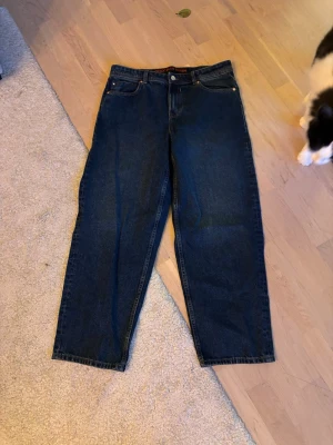 Mörkblå raka jeans - Säljer ett par mörkblå jeans med rak passform och klassisk femficksdesign. Jeansen har hög midja och stängs med knapp och dragkedja. Perfekta för en avslappnad och stilren look.