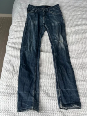 Mörkblå raka jeans med slitningar - Säljer ett par mörkblå jeans med raka ben och snygga slitningar på framsidan. Jeansen har klassisk femficksdesign och kontrastsömmar. Perfekta för en avslappnad och trendig look. Materialet är denim i bomull.