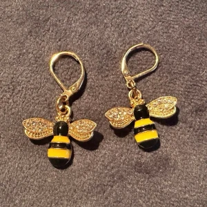 Örhängen med Bin - Snygga örhängen i form av bin, svarta och gula ränder samt gnistrande stenar på vingarna. Hängande modell med smidig låsanordning. Perfekta för dig som vill sticka ut med en lekfull accessoar. I fint skick, aldrig använda!