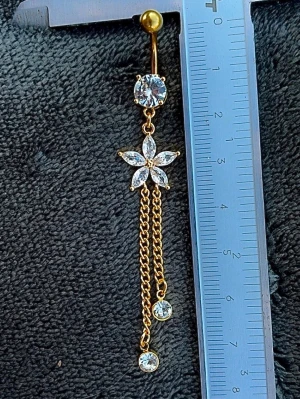 NY oanvänd Navelpiercing med långt hänge | Kirurgiskt stål | Blomma, kedjor och vita stenar  - 💕30% Bundle-rabatt vid köp av minst 2 artiklar. ⭐️NY oanvänd piercing i kirurgiskt stål; rostfritt och säkert för läkta piercingar.                               📏MÅTT ⭕️Stavens längd: 10mm ⭕️Stavens tjocklek: 1,6mm  ⭕️Smyckets totala längd: 80mm                                                                          🤍Färger: Guld och vit                                                             💌Skickas spårbart via Plick SafePay.