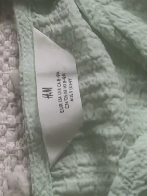 Mintgrönt set från H&M - Säljer ett mintgrönt set från H&M med croppad topp och vida byxor i mjukt, krinklat tyg. Toppen har smala axelband och knytning framtill, medan byxorna har resår i midjan för skön passform. Perfekt för en avslappnad och trendig look.