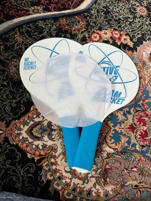Strandtennisset från Active - Strandtennisset med två vita racketar med blå handtag och tryck. Setet innehåller även plastbollar och färgglada fjädrar i en genomskinlig påse. Perfekt för utomhusspel och häng med vänner.
