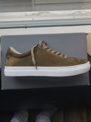 Olivgröna mockasneakers från Vagabond - Snygga olivgröna sneakers från Vagabond i mocka med vita sulor och matchande olivgröna skosnören. Klassisk låg modell med stilren design och rundad tå. Perfekta för dig som gillar en clean och modern look. Helt nya och har bara provat på de 1 gång.