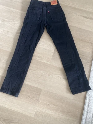 Svarta Levi's 501  jeans raka ben - Säljer ett par svarta jeans från Levi's med raka ben och klassisk femficksdesign. Jeansen har en läderpatch bak i midjan och kopparfärgade nitar fram. Materialet är denim i bomull. Perfekta för en avslappnad och stilren look.