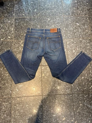 Mörkblå jeans tiger of Sweden  30/32 - Säljer ett par mörkblå jeans från tiger of Sweden modellen Impulse. Klassisk femficksdesign, raka ben och snygga kontrastsömmar. Tillverkade i bomull och har en läderpatch bak i midjan. Perfekta för en avslappnad och stilren look.
