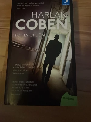 För evigt dömd av Harlan Coben - Spännande kriminalroman av Harlan Coben i pocketformat. Omslaget är mörkt med en siluett av en man i en korridor. Boken handlar om en försvunnen sjuttonårig flicka och en journalist som jagar sanningen. Perfekt för dig som gillar thrillers och mysterier.