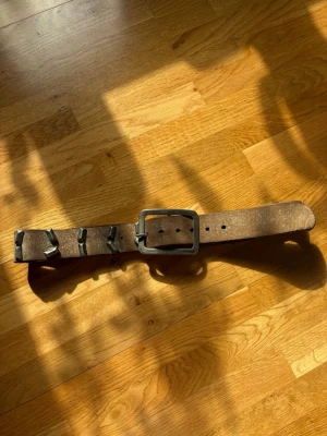 Vintage från Aloe & Wolf - Säljer ett brunt skärp i skinn med fyrkantigt metallspänne och dekorativa metallöglor. Bältet har en rå och robust look som passar till jeans eller byxor. Köpt på en vintage butik i Italien. 
