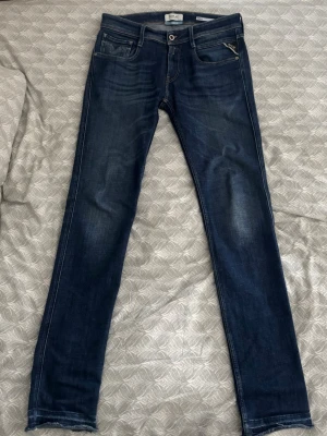 Mörkblå anbass jeans från Replay - Snygga mörkblå slim fit jeans från Replay med klassisk femficksdesign och diskreta slitningar framtill. Jeansen har dragkedja och knapp i midjan samt Replay-lapp bak i midjan. Materialet är stretchigt denim som sitter tight och bekvämt.