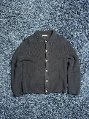 Mörkblå kofta - Stilren mörkblå ribbad kofta med klassisk krage och knäppning framtill. Koftan har långa ärmar och en mjuk, strukturerad yta som ger en avslappnad men ändå snygg look. Perfekt att slänga över en t-shirt eller bära stängd. Sitter lite mer som en S. Hör av er vid minsta fundering!